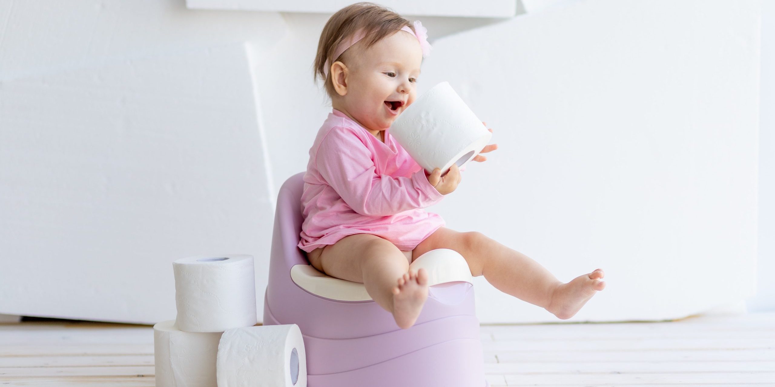 little-girl-sitting-white-room-potty-pink-clothes-with-toilet-paper-min
