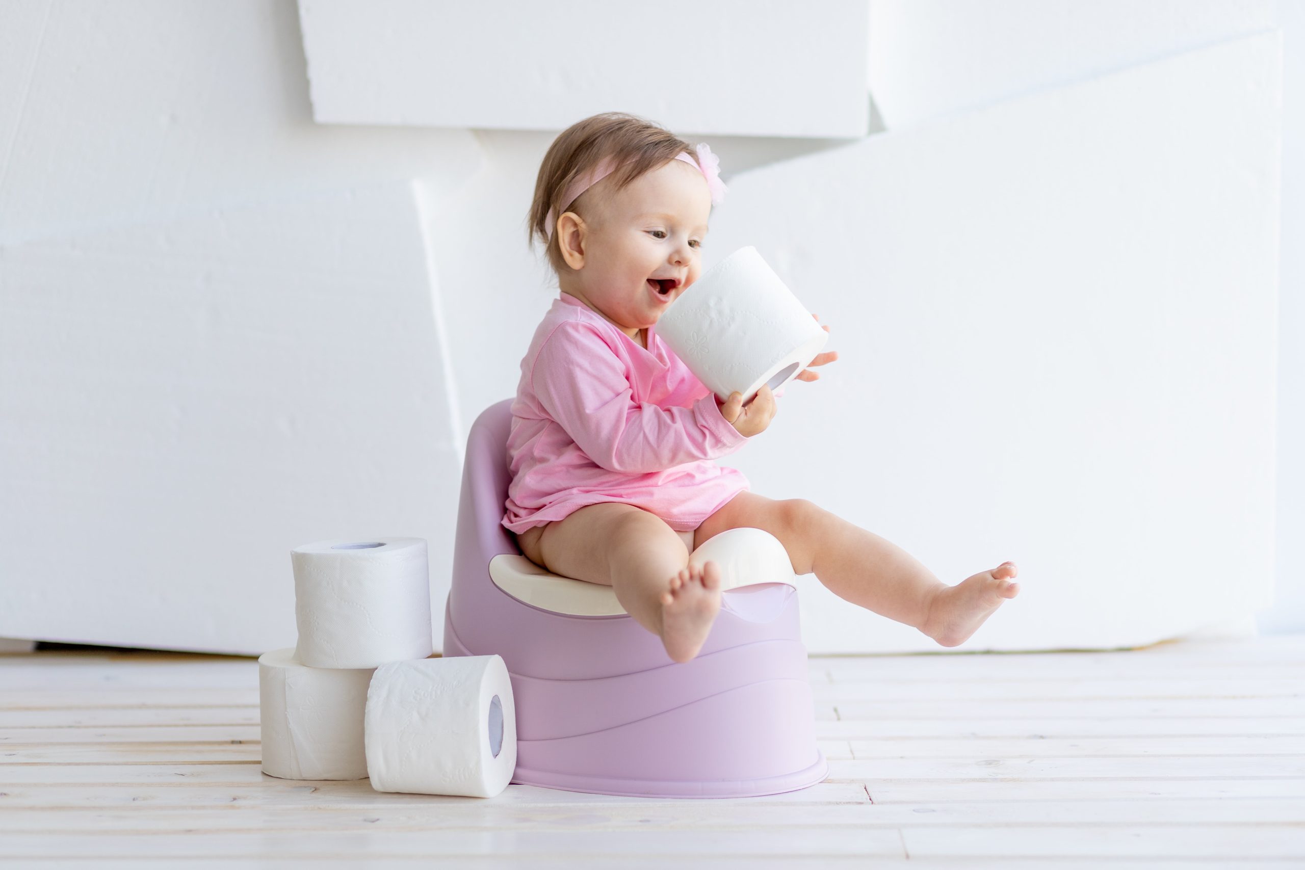 little-girl-sitting-white-room-potty-pink-clothes-with-toilet-paper-min